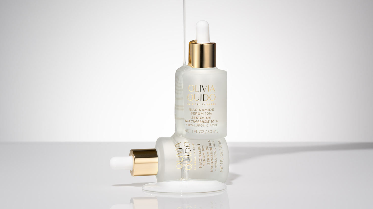 Olivia Quido Niacinamide Serum 10% sitting on top of another bottle of Niacinamide with serum dripping over
