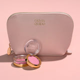 Olivia Quido Faux Leather Dome Cosmetic Bag with makeup products on a pink background.
